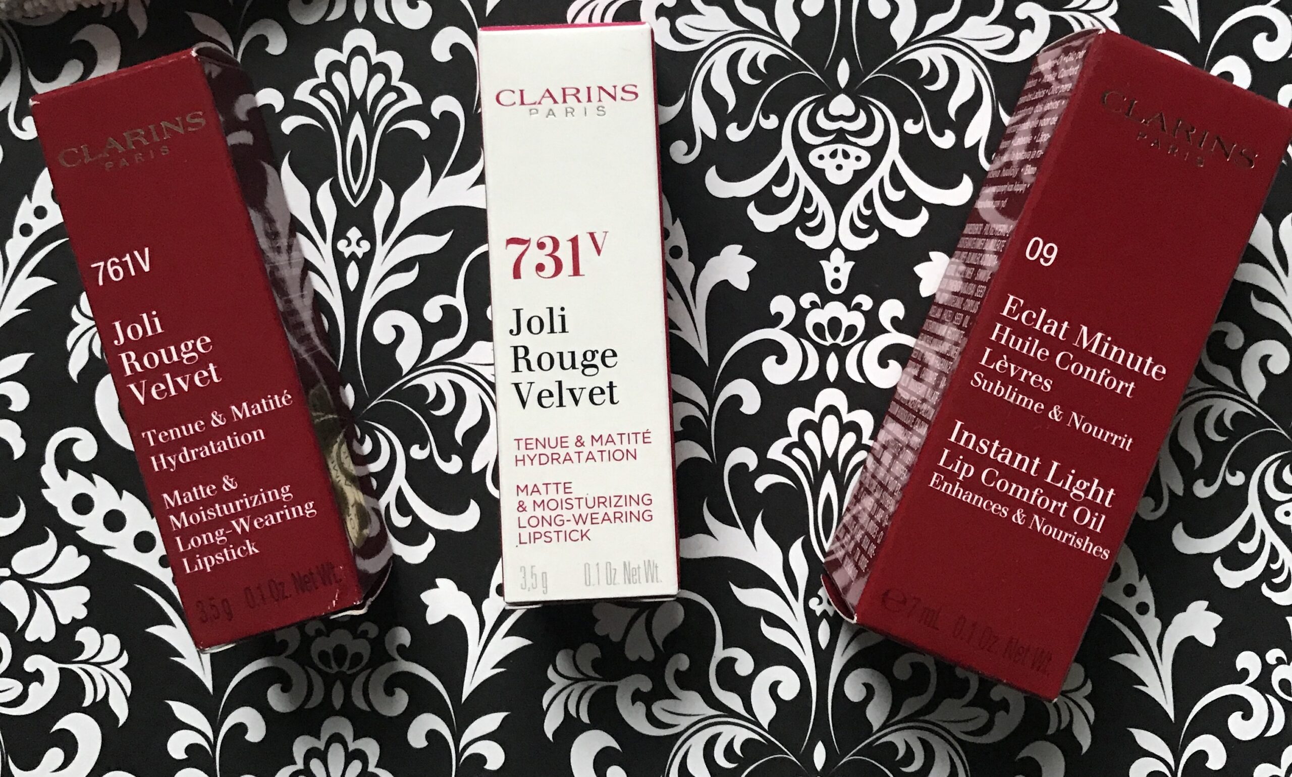 closeup of the outer boxes of three Carlins lip products: two Joli Rouge Velvet Lipstick boxes and a box of Instant Light Lip Comfort Oil, neversaydiebeauty.com