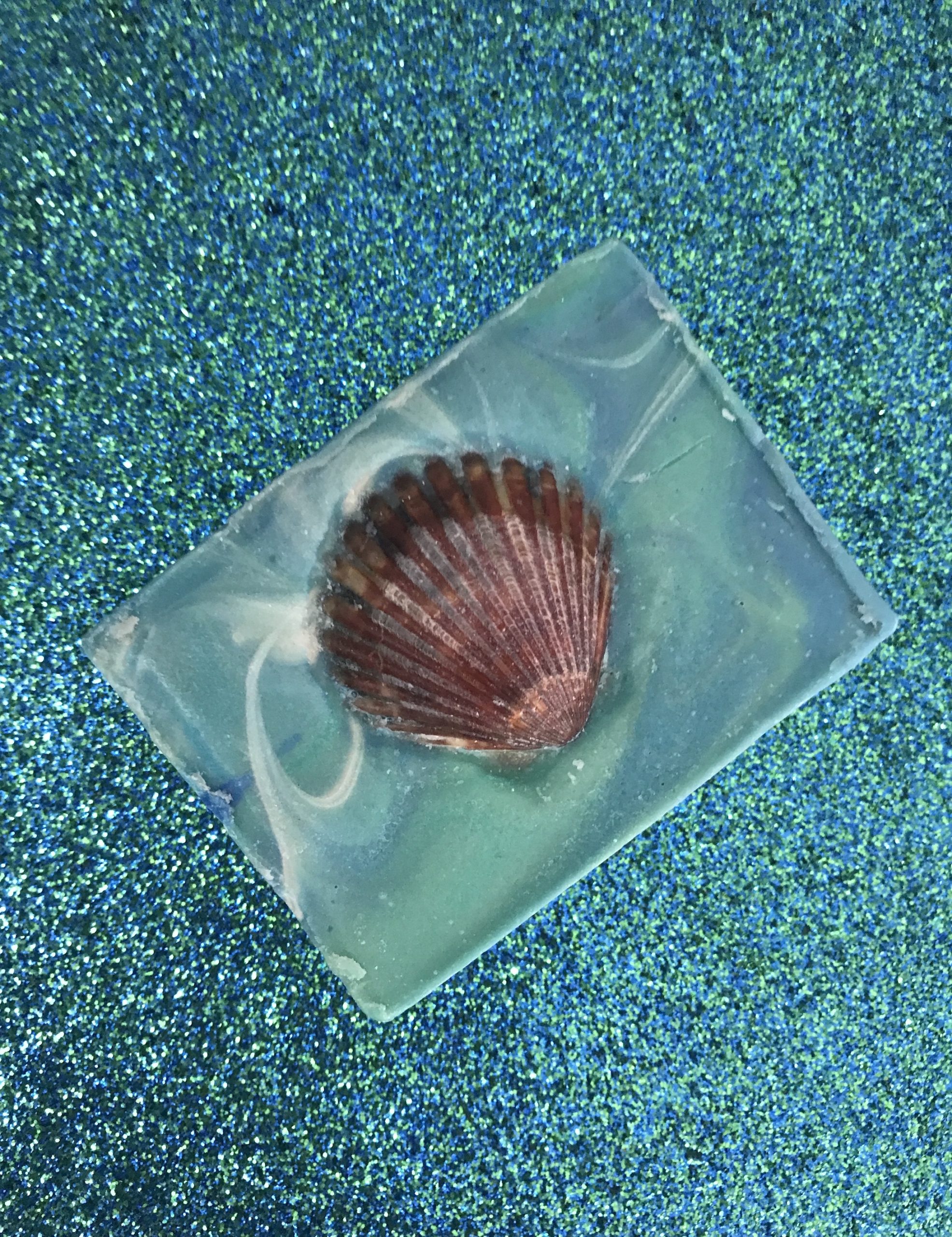 turquoise and blue swirled bar soap with scallop shell on a turquoise glitter background